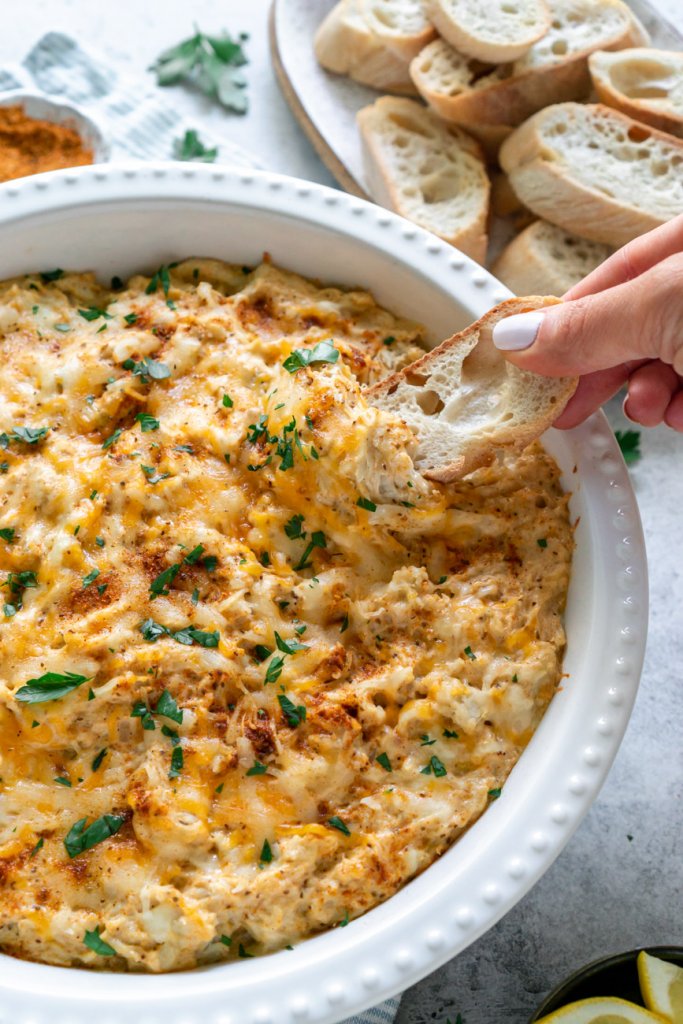 a hand dipping toasted baguette in crab dip.