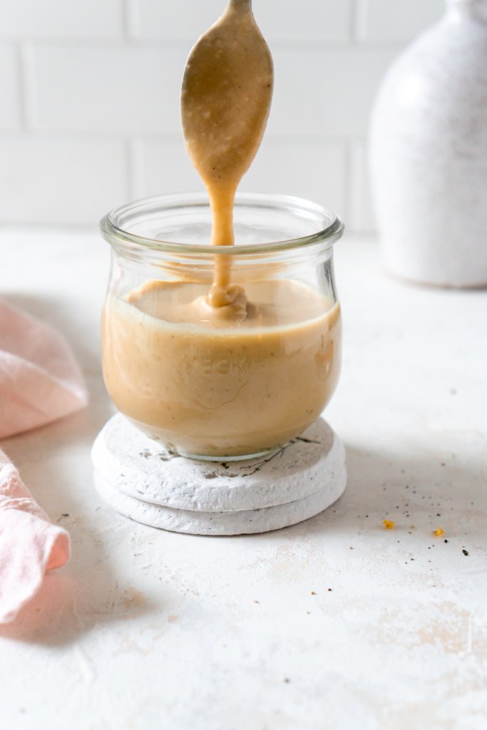 a spoon dipping into a glass jar with miso tahini sauce