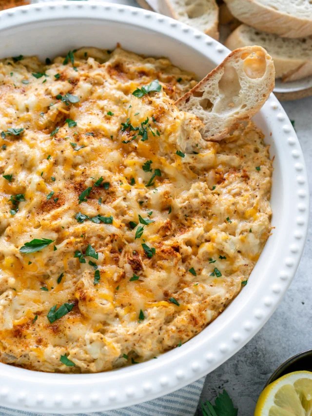A bowl of crab dip with a piece of bread.