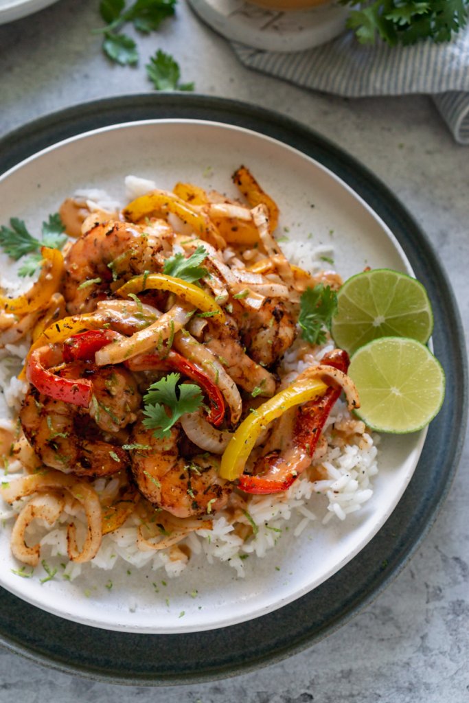 air fryer shrimp and peppers on a white plate with limes