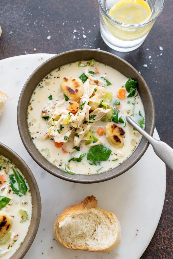two bowls of soup, one with a spoon and a piece of bread on the side