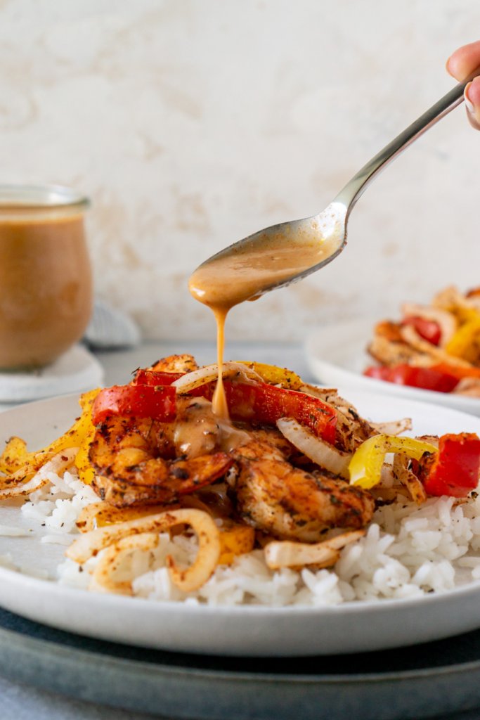 a spoon drizzling coconut curry sauce over shrimp and peppers
