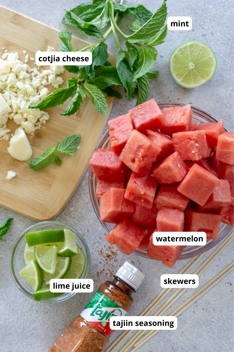 Cubed watermelon, fresh mint, lime wedges, tajin, crumbled cotija on a gray background.