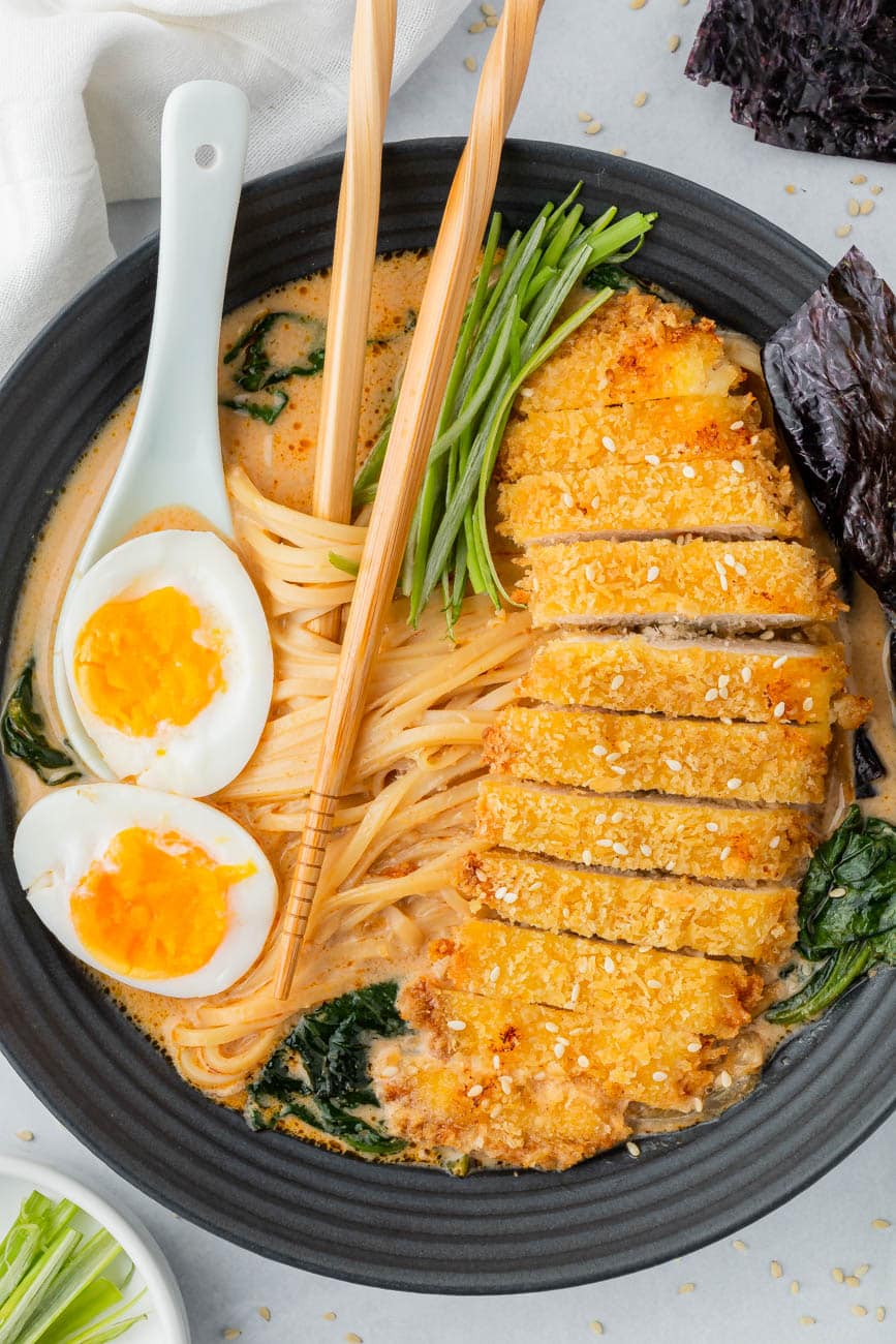 Chicken katsu ramen in a black bowl with chopsticks and a soft boiled egg on top.