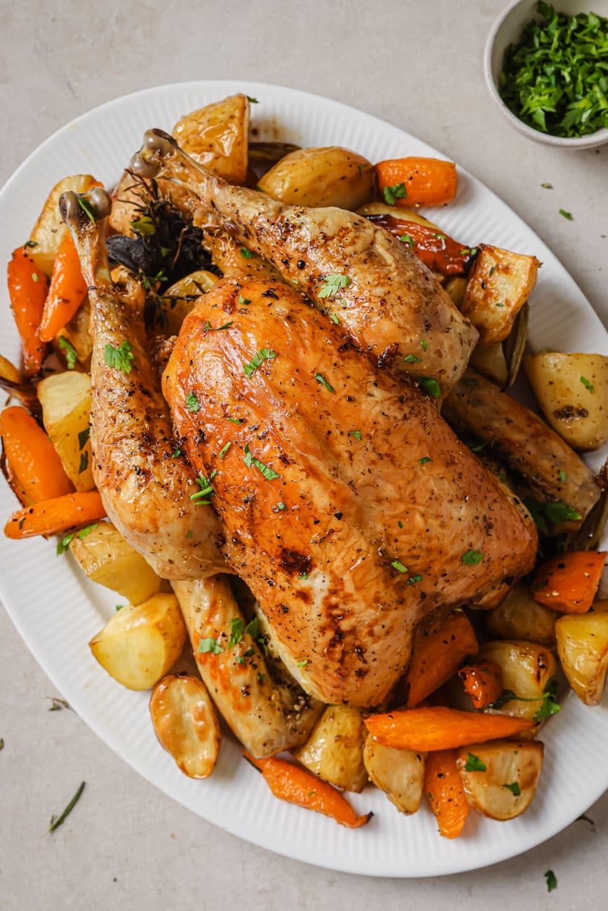 Slow roasted chicken on a white serving platter with carrots and potatoes.
