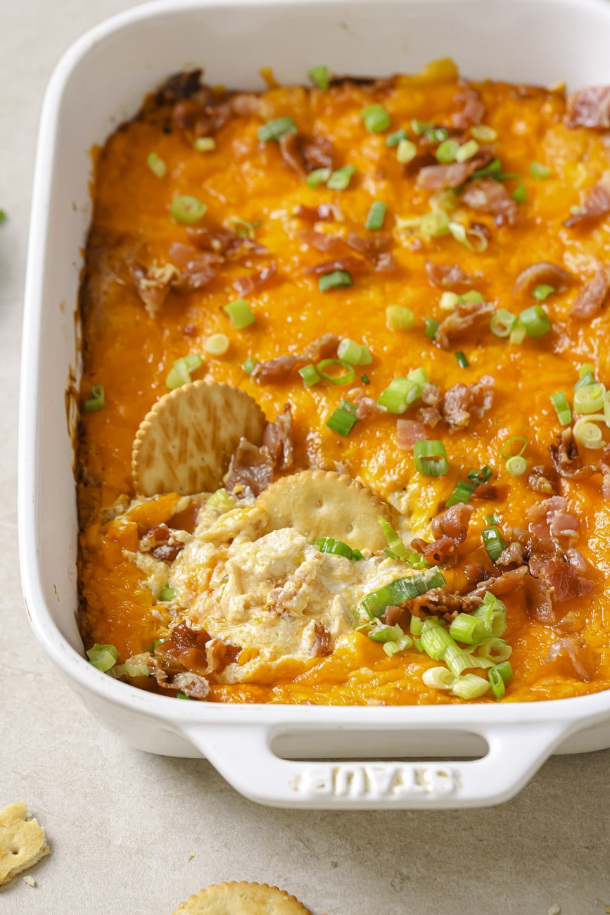 crack chicken dip in a white baking dish with two ritz crackers dipped inside