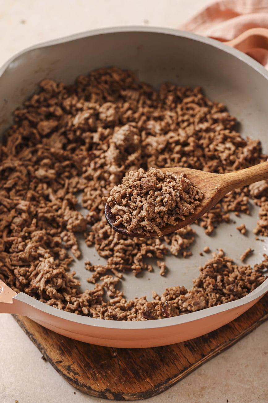 Browned ground beef in a skillet with a wooden spoon.