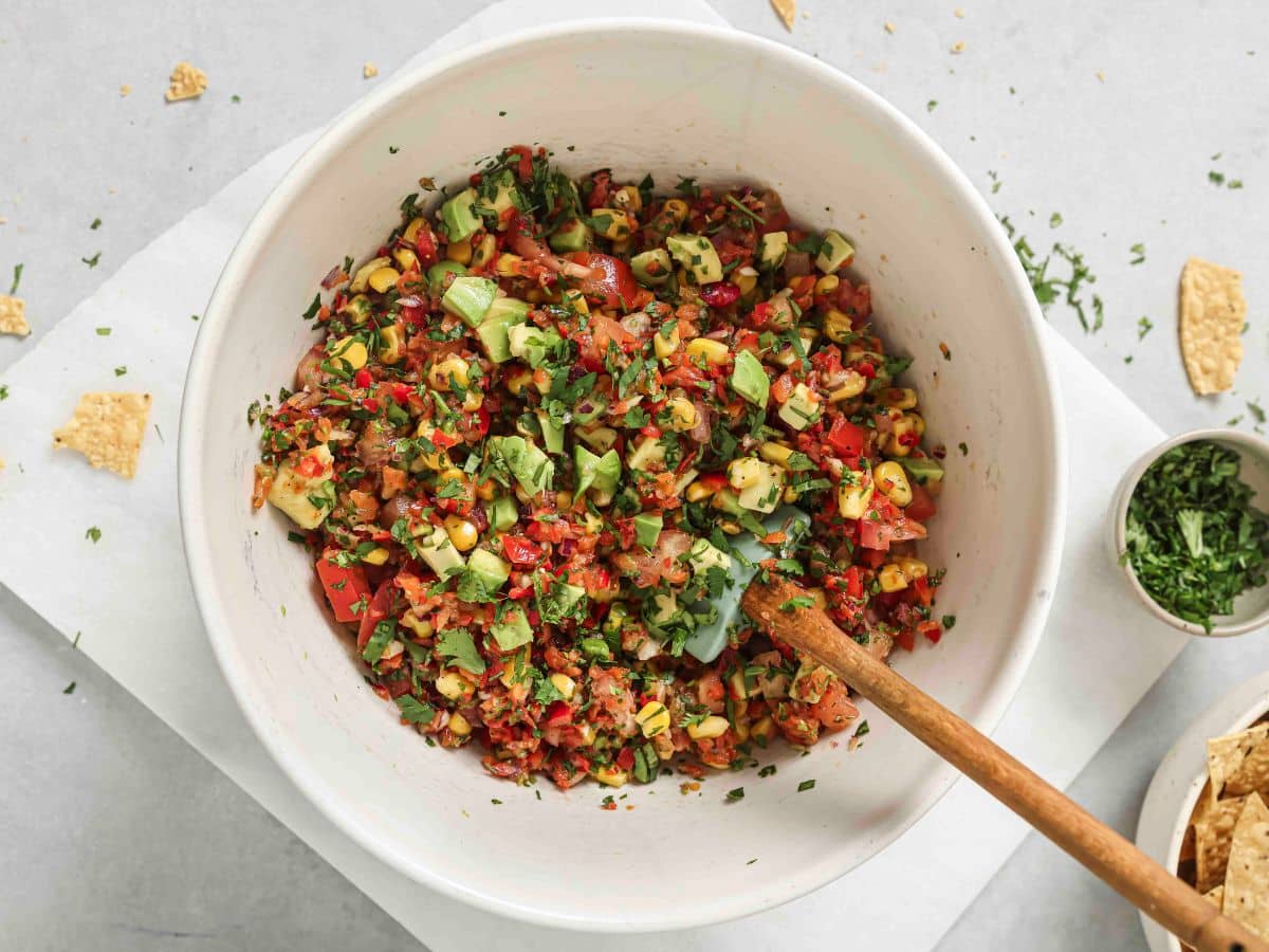 Corn salsa in a white bowl with cilantro, avocado, tomatoes, and fresh lime juice. 