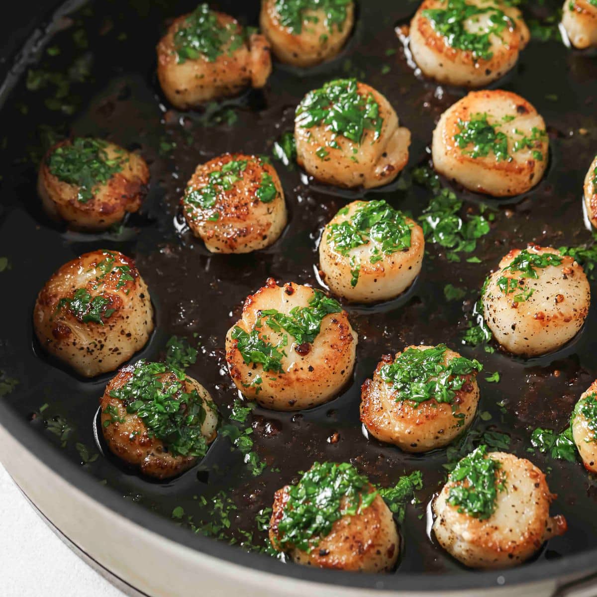 Pan-seared scallops topped with parsley butter in a black pan.