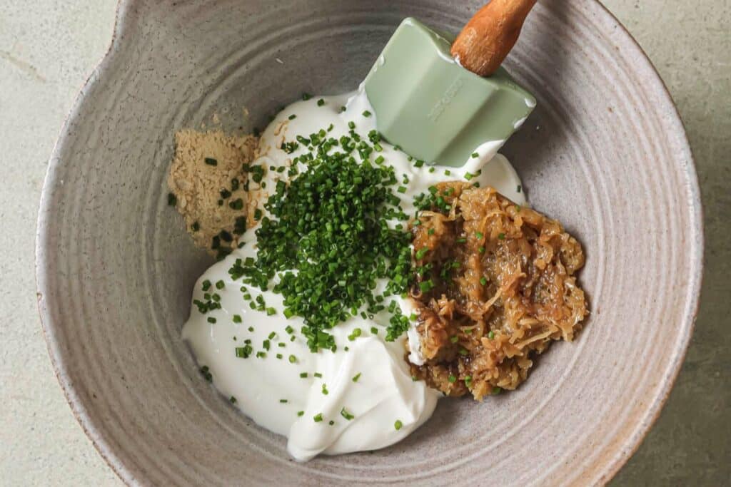 A mixing bowl filled with all of the ingredients for french onion dip.
