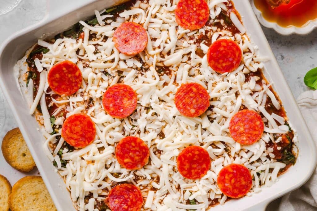 Cheese and mini pepperonis added to the top of the sauce and basil to form the last layer of the pizza dip recipe.