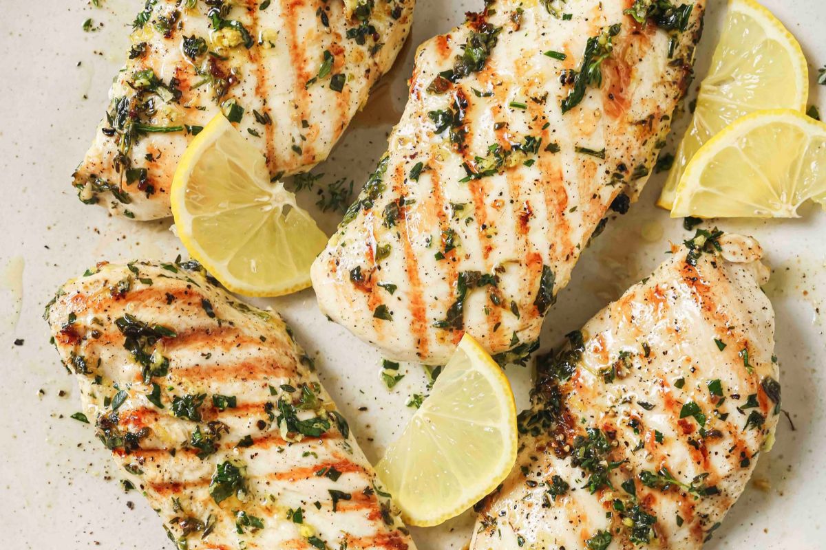 Grilled lemon herb chicken breasts on a plate with lemon wedges.