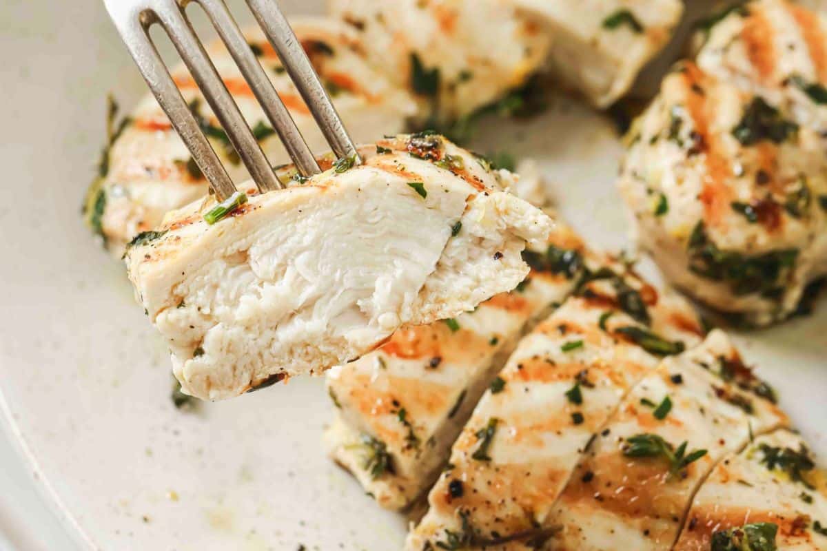 A fork holding up a piece of lemon herb chicken showing the center is white and not pink.