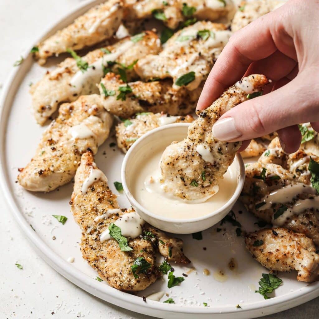 Dipping air fryer chicken tenders in dressing.