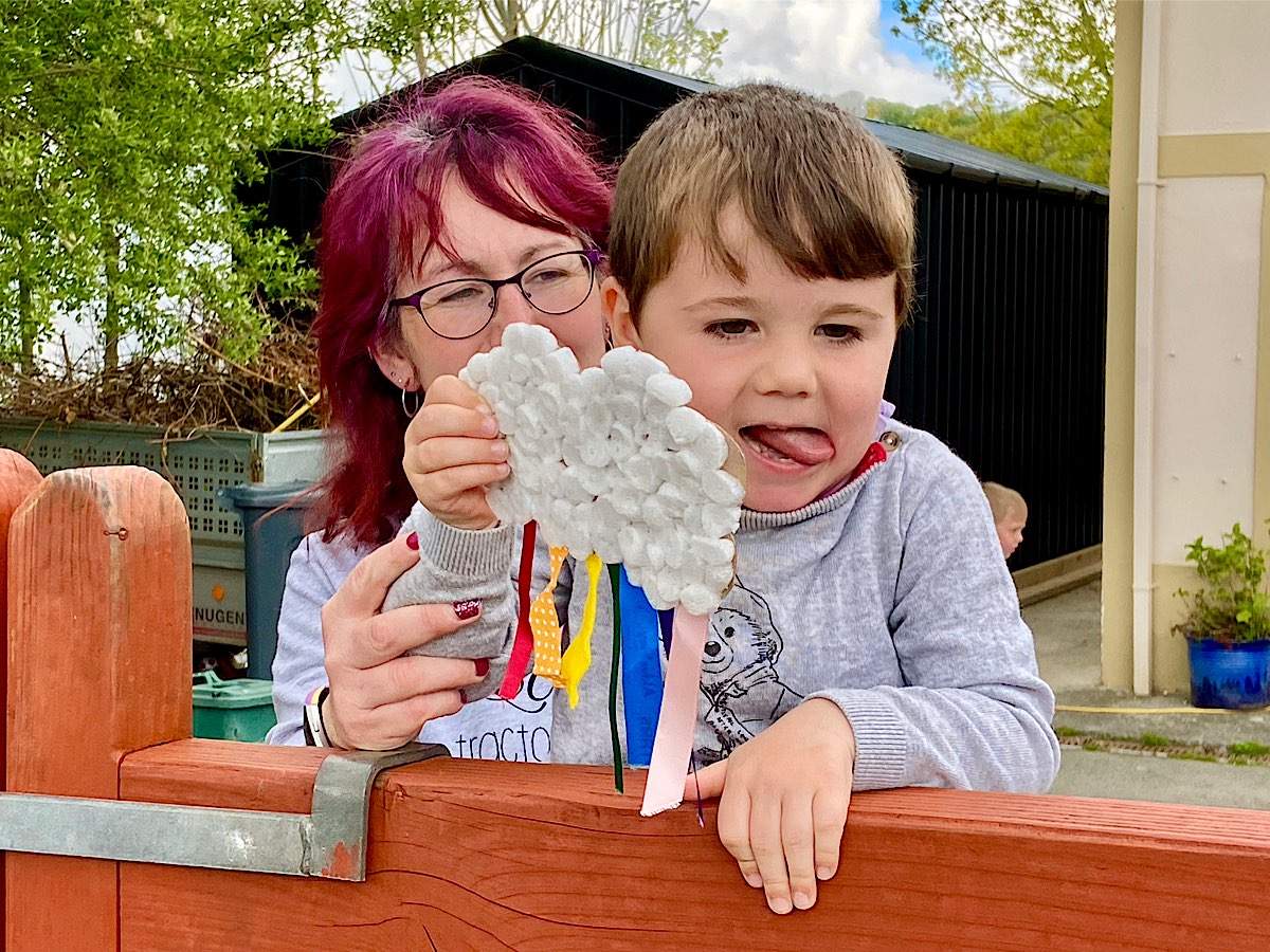 A mother holds up her little boy at the gate - he is holding a cloud with rainbow strings hanging down. It was very creative