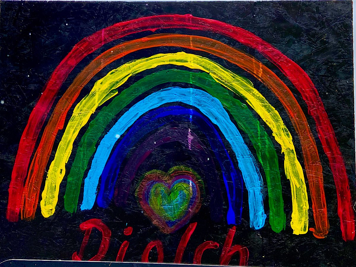 A rainbow painted on black board, says 'diolch' underneath and a small heart shaped also rainbow coloured heart sits under the rainbow