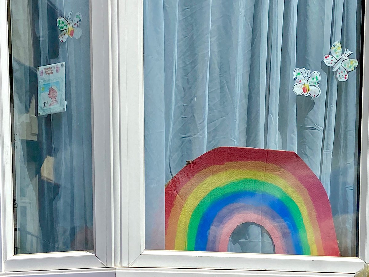 A cut out rainbow in a window surrounded by colourful butterflies