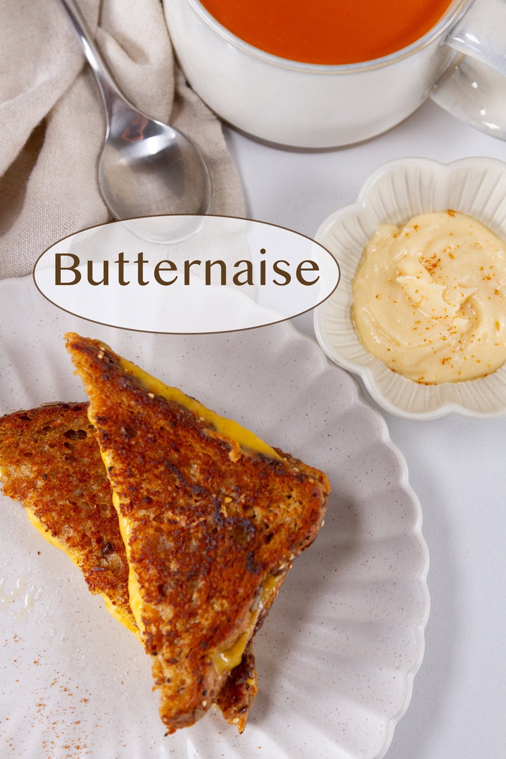 a grilled cheese sandwich with a cup of tomato soup and a small dish of Butternaise.