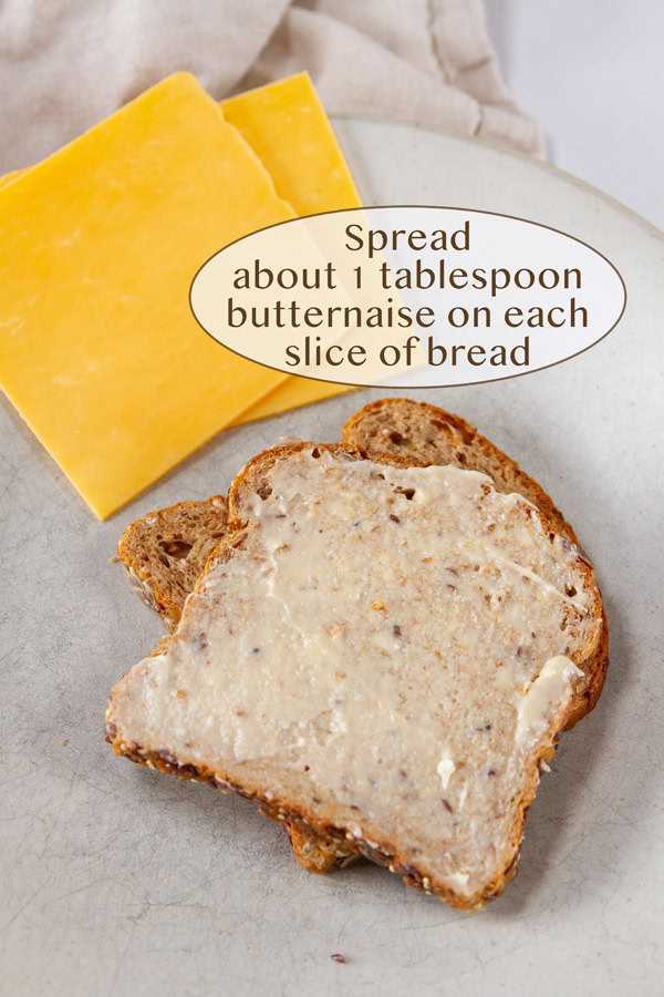 two slices of cheese next to two slices of bread, one with spread on it.