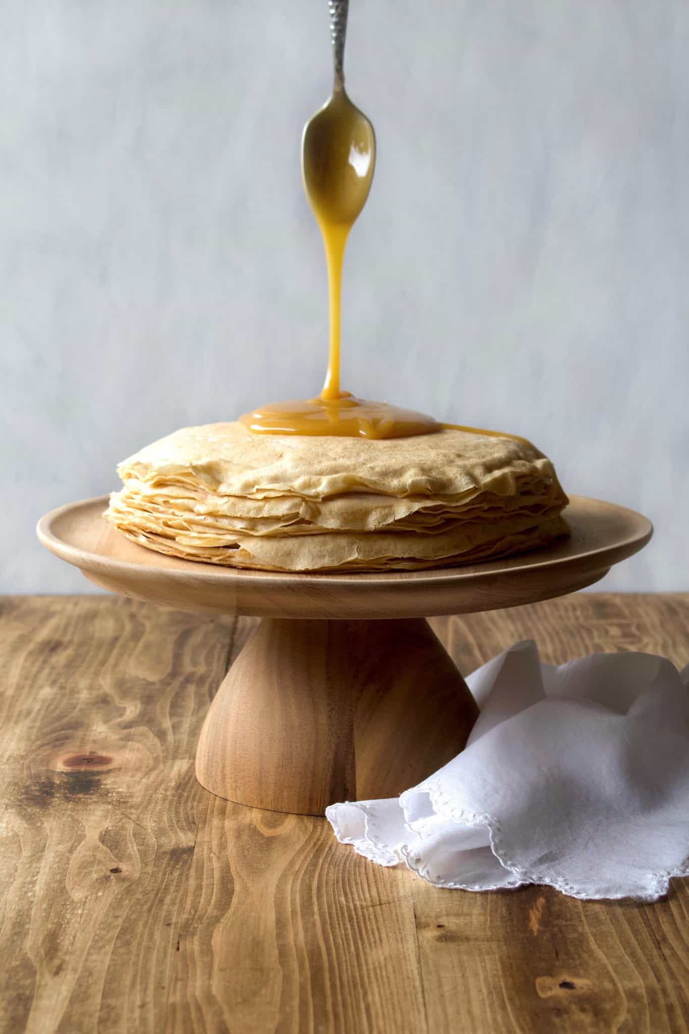 Coconut whipped cream sandwiched between layers of delicious crêpes, then topped with rich homemade dulce de leche! Whether you call it gâteau de crêpes, mille crêpe, or crepe cake, this is a beautiful and impressive dessert! #french #crepecake #crepes #pancakes #gateau #millecrepe #dulcedeleche #coconut #dairyfree #condensedmilk #caramel #cake