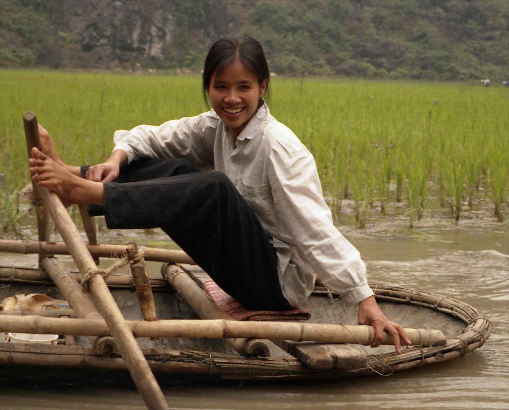 Pretty woman rowing her bamboo mat boat with her feet; Hoa Lu, Red