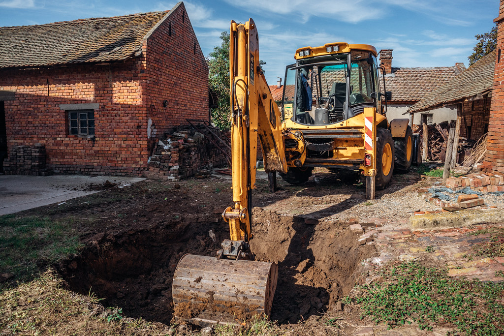 Backhoe digging a hole in the ground next to an old unfini… Flickr