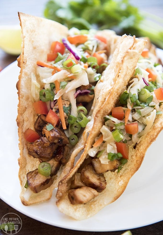 Two teriyaki chicken wonto tacos topped with green onion, bell pepper, and carrots.