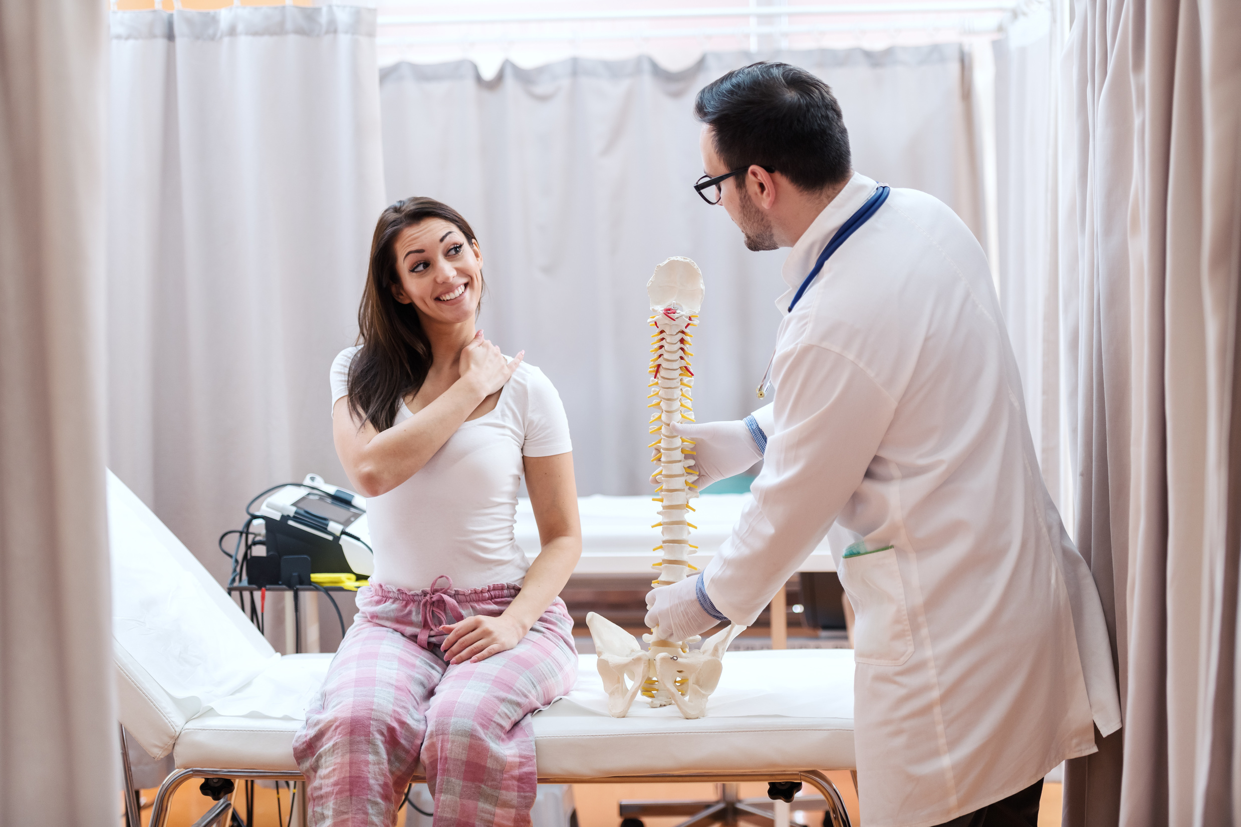 Female patient in pajamas sitting on hospital bed and showing hurting