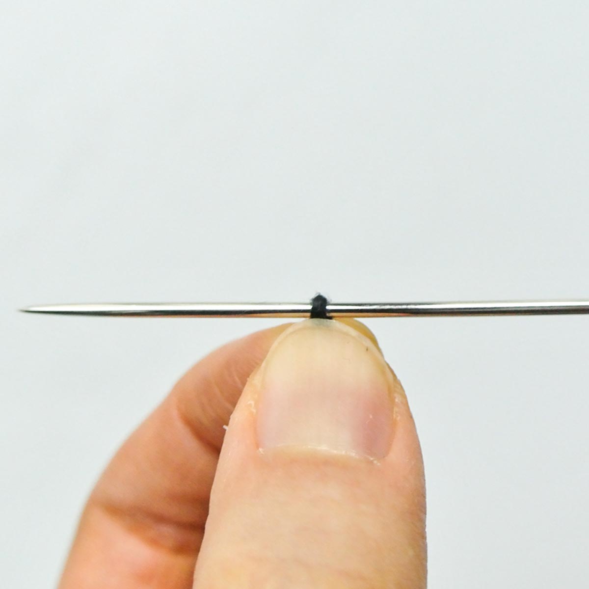 Hands pinching looped thread over needle. 