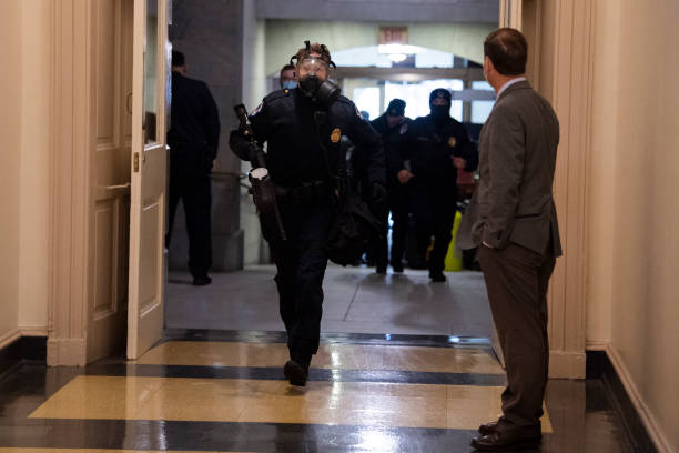 A U.S. Capitol Police officer runs from a door leading to the west front as rioters attempt to break into the Capitol to disrupt the joint session of Congress to certify the Electoral College vote on Wednesday, January 6, 2021. Rep. Chris Stewart, R-Utah, appears at right. (Photo By Tom Williams/CQ-Roll Call, Inc via Getty Images)