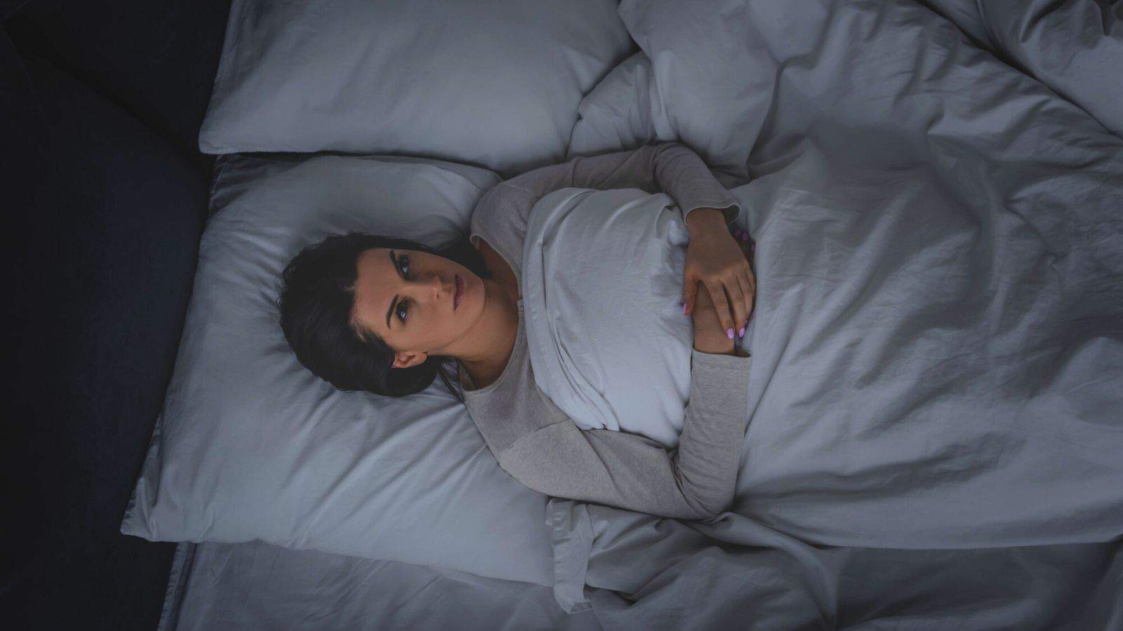 Woman looking up at the ceiling while lying down on bed at night