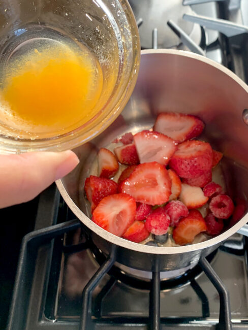 Hand adding citrus to berries in saucepan.