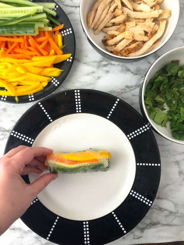 Showing the finished roll, you can see bell pepper and mango slices through the rice wrapper. Other ingredients nearby.