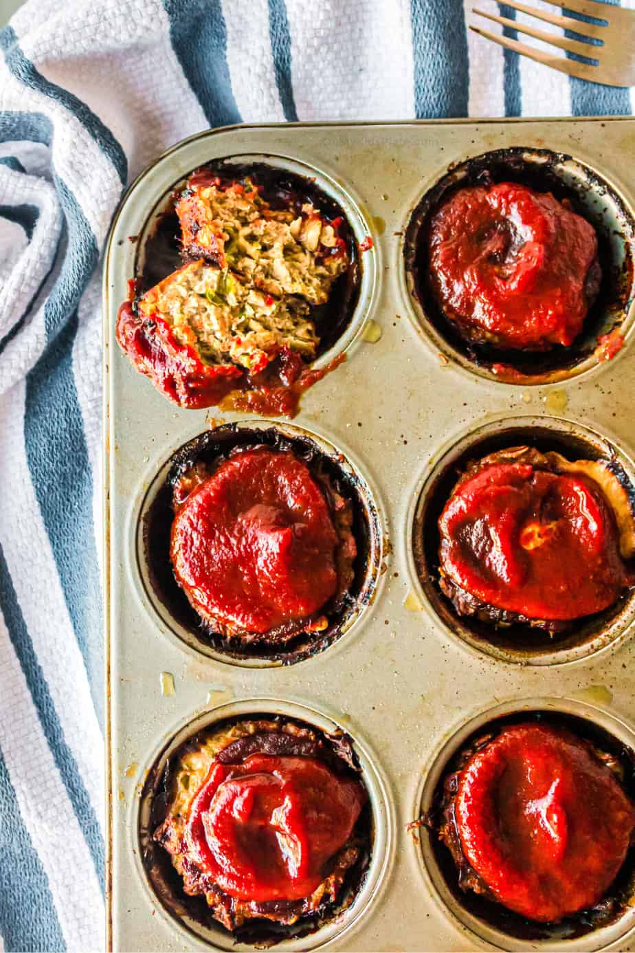 Mini meatloaf from overhead in the muffin pan with one sliced in half to see inside.