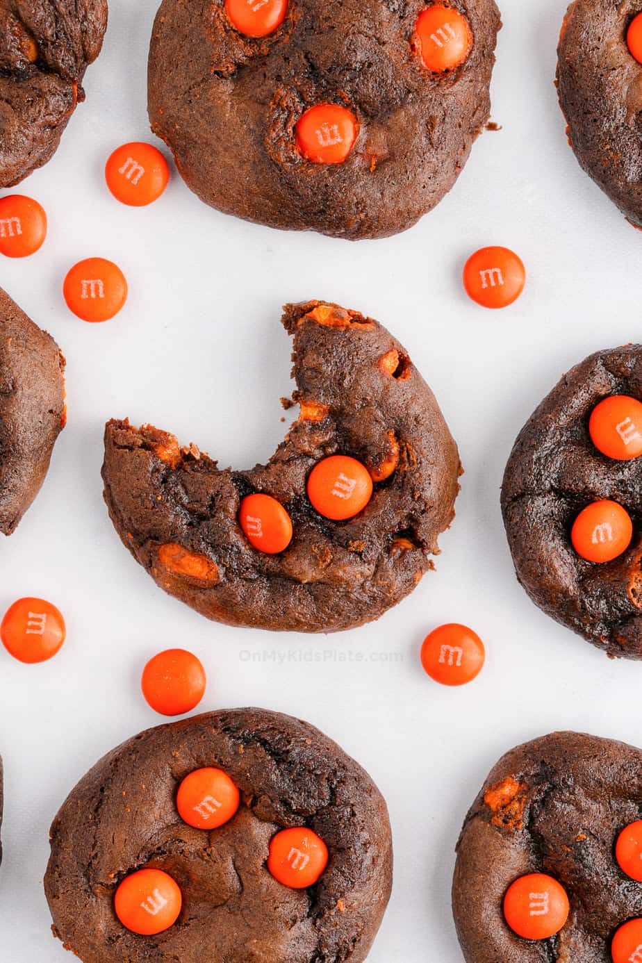 Chocolate cookies with orange chocolate candies spaced on a counter with the middle cookie missing a bite.