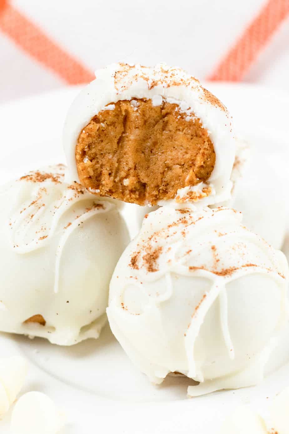 Round pumpkin cheesecake truffles stacked on a plate from the side close up with the top piece missing a bite.