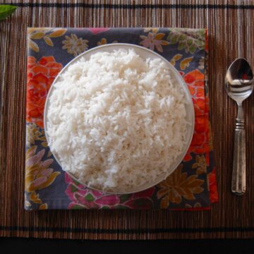 Instant Pot Jasmine Rice in white bowl on straw placemat with colorful napkin and a spoon - Paint the Kitchen Red