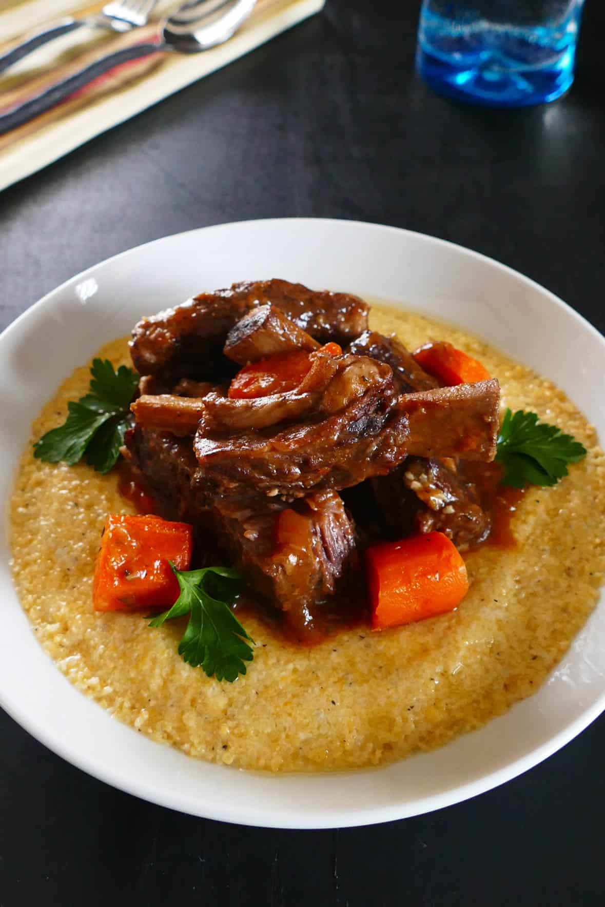 Instant Pot Short Ribs in white bowl over polenta, with carrots