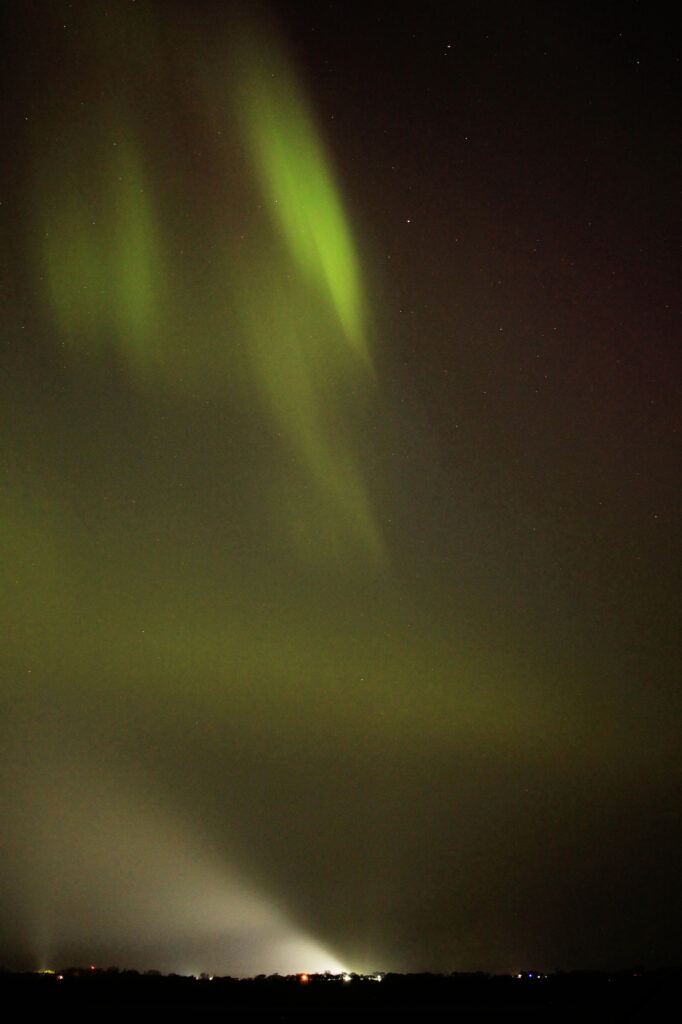 Aurora above a building's bright light, its beam visible in the smoke