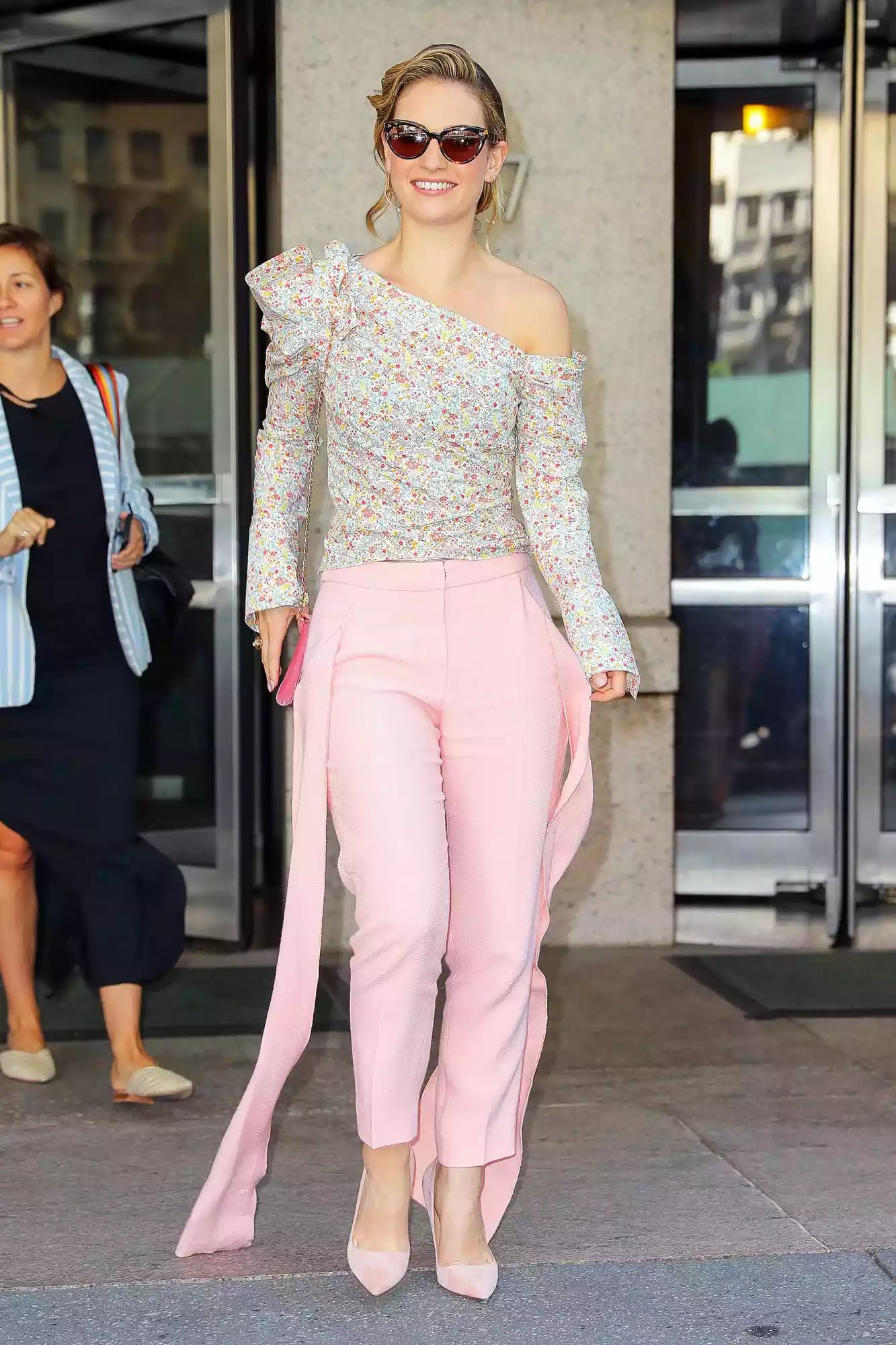 Lily James wears a long sleeve one shoulder-off flowered top with pink pants as leaving the ABC studios