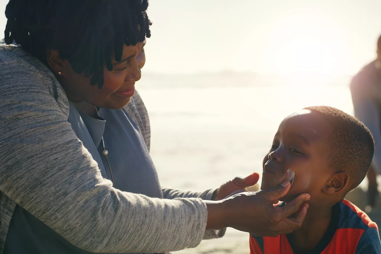 Cropped shot of an attractive senior woman putting sunblock on her cute grandson as they play on the beach
