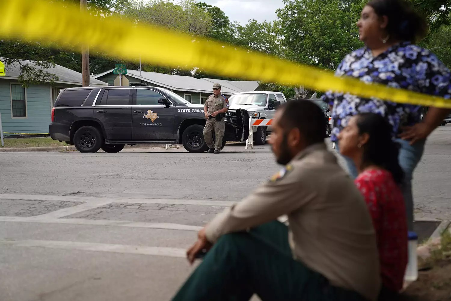 People sit on the curb outside of Robb Elementary School as State troopers guard the area in Uvalde, Texas, on May 24, 2022. - An 18-year-old gunman killed 14 children and a teacher at an elementary school in Texas on Tuesday, according to the state&rsquo;s governor, in the nation&rsquo;s deadliest school shooting in years.