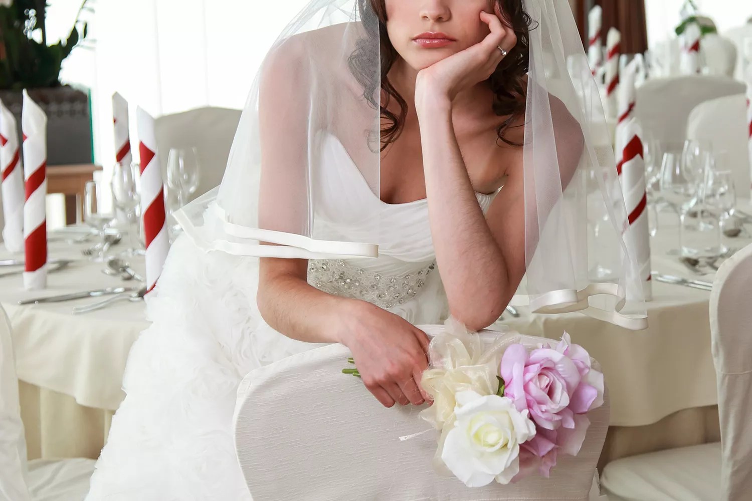 Bride sitting in a ceremony waiting restaurant. Sitting sad with head and flowers in her hands.