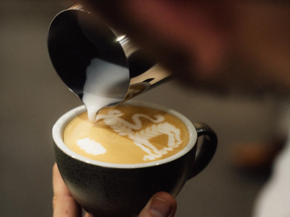 - Healthy Brew Hub A barista pours latte art on a milk-based coffee drink.