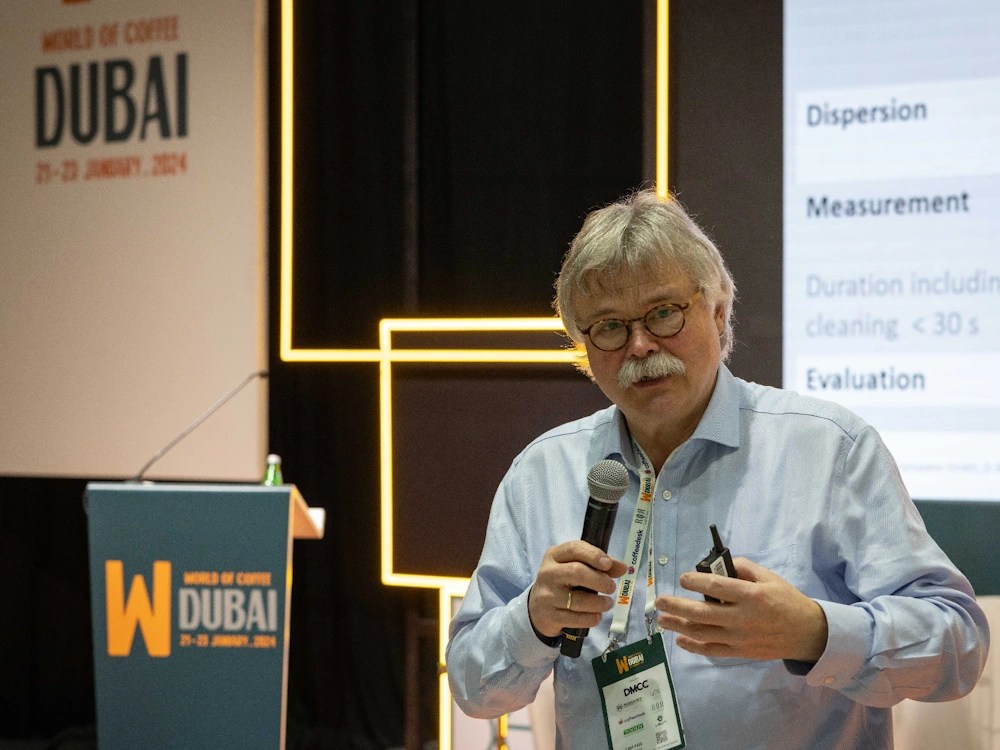 - Healthy Brew Hub A coffee professional leads a lecture at the World of Coffee Dubai 2024 event.