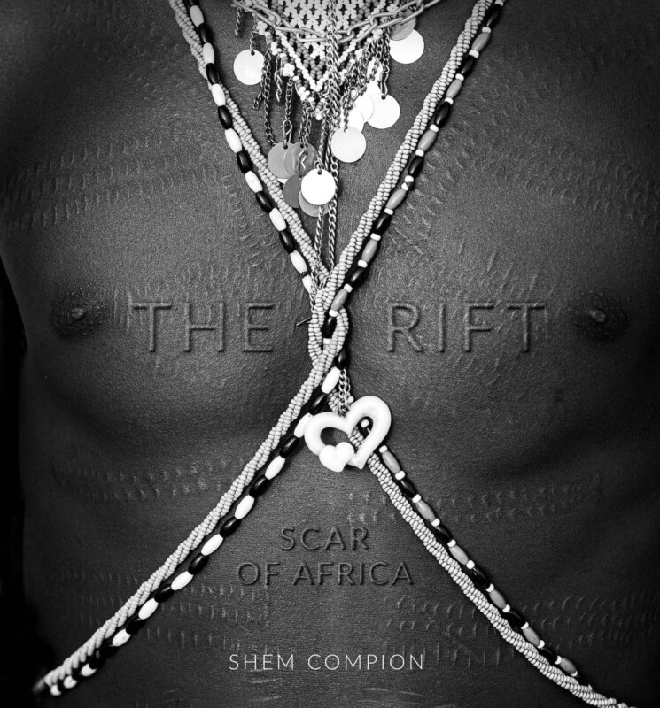 Black-and-white photo of a person's chest adorned with beaded necklaces and jewelry; intricate raised scarification marks are visible, with the words