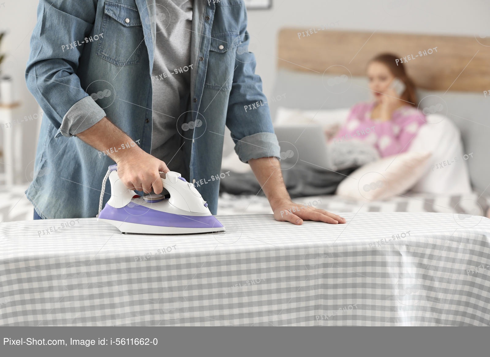 Househusband ironing clothes while his wife working in bed Stock
