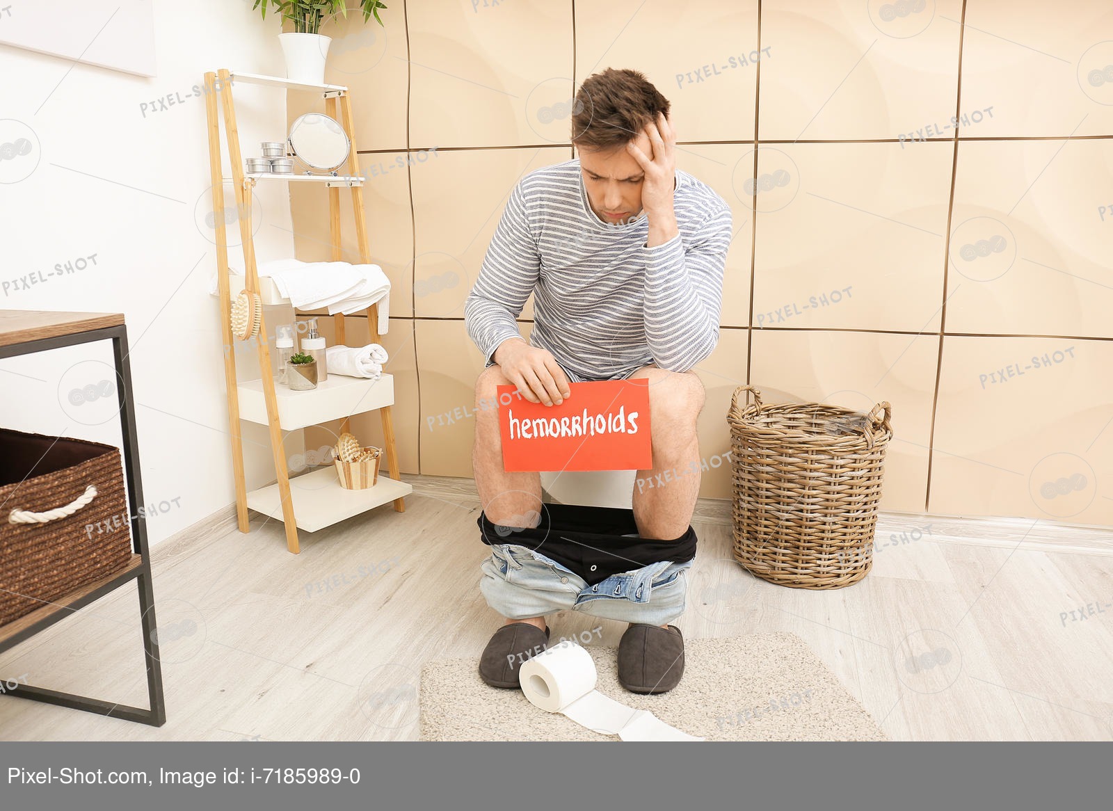 Young man with hemorrhoids sitting on toilet bowl in restroom Stock