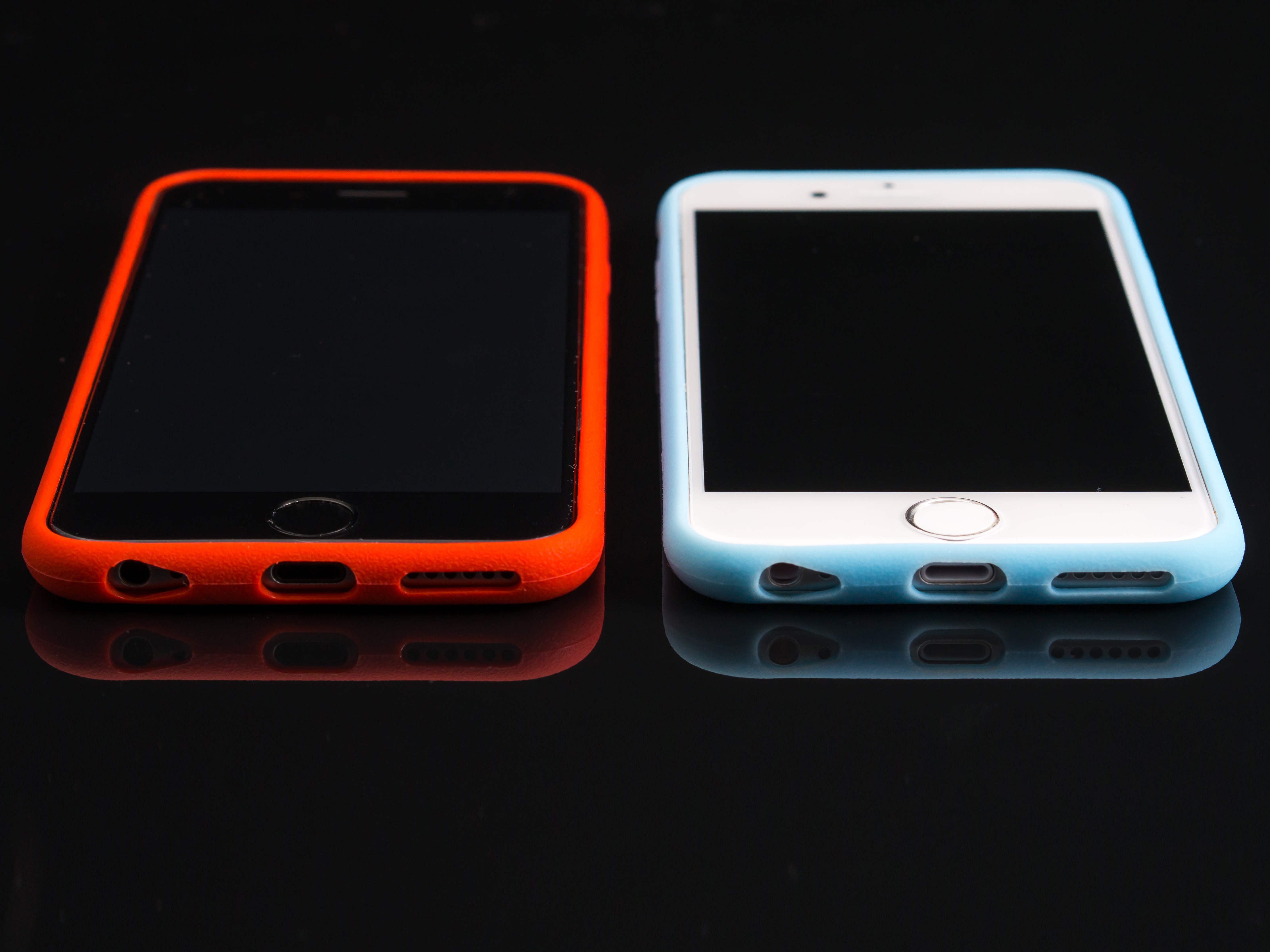 Two beautiful, black and white Iphones with red and turquoise cases on