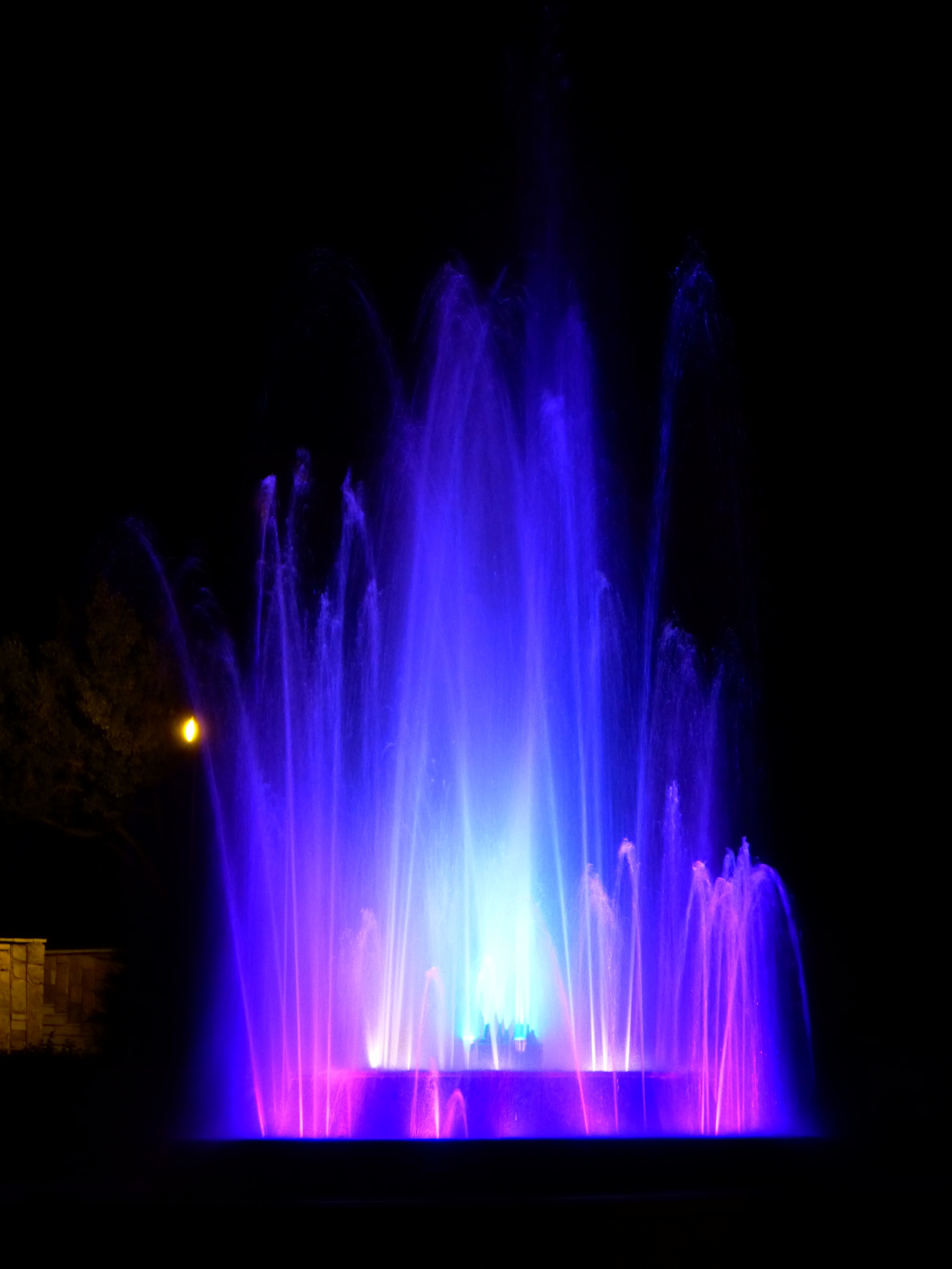 Beautiful fountain with colorful lights, among the darkness, at the